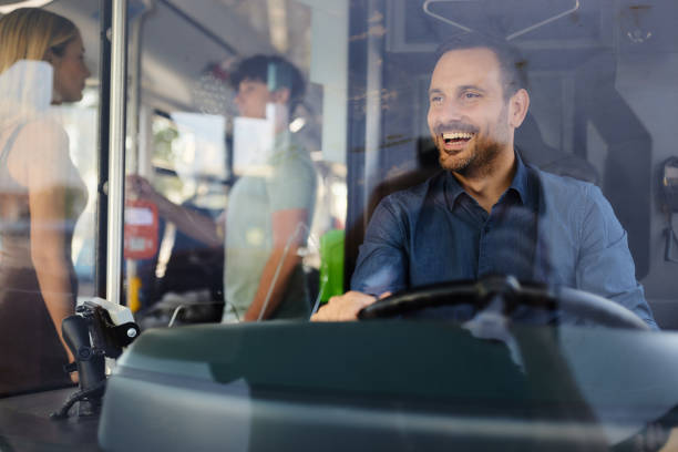Happy male driver enjoying while driving a bus with his passengers. The view is through glass.